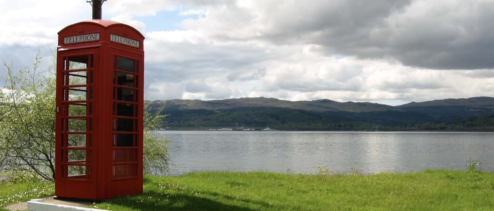 Red telephone booth on grassy hill next to a lake